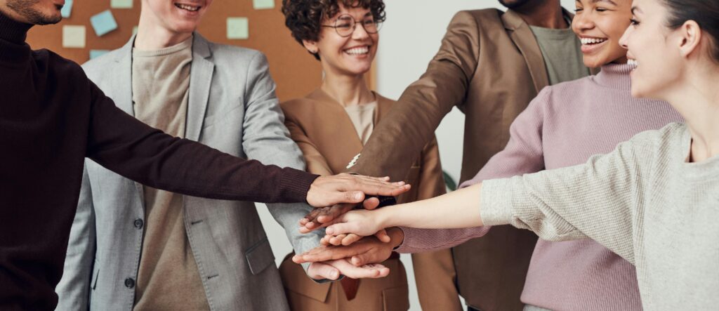 pexels-photo-3184424-3184424 A group of happy, diverse colleagues celebrating teamwork and cooperation with a group high five indoors.